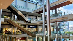 A multi-level shopping mall with glass railings, escalators, and a clear view of the sky.
