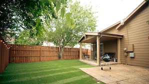 A backyard with a patio, a covered seating area, a barbecue grill, and a wooden fence.