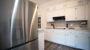 A modern kitchen with stainless steel appliances, white cabinetry, and a tiled backsplash.