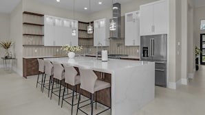 Una cocina moderna con una isla grande, taburetes de bar, electrodomésticos de acero inoxidable e iluminación colgante.