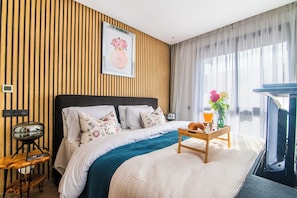 A hotel room with a bed, a wooden side table with a croissant and a glass of orange juice, a framed picture on the wall, and a view of the outdoors through sheer curtains. - DAR DYAFA VIP (Agadir)