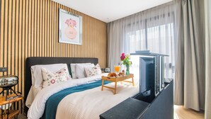 Una habitación de hotel con una cama, una mesita de noche, un televisor y una ventana con cortinas.