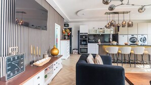 Una cocina moderna con una isla central, un comedor con taburetes de bar y una sala de estar con un sofá oscuro.