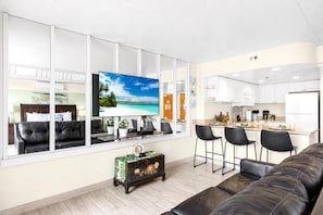 Ein modernes Wohnzimmer mit großem Fernseher, einer Couch, einem Couchtisch und einer Küchenzeile mit Barhocker.