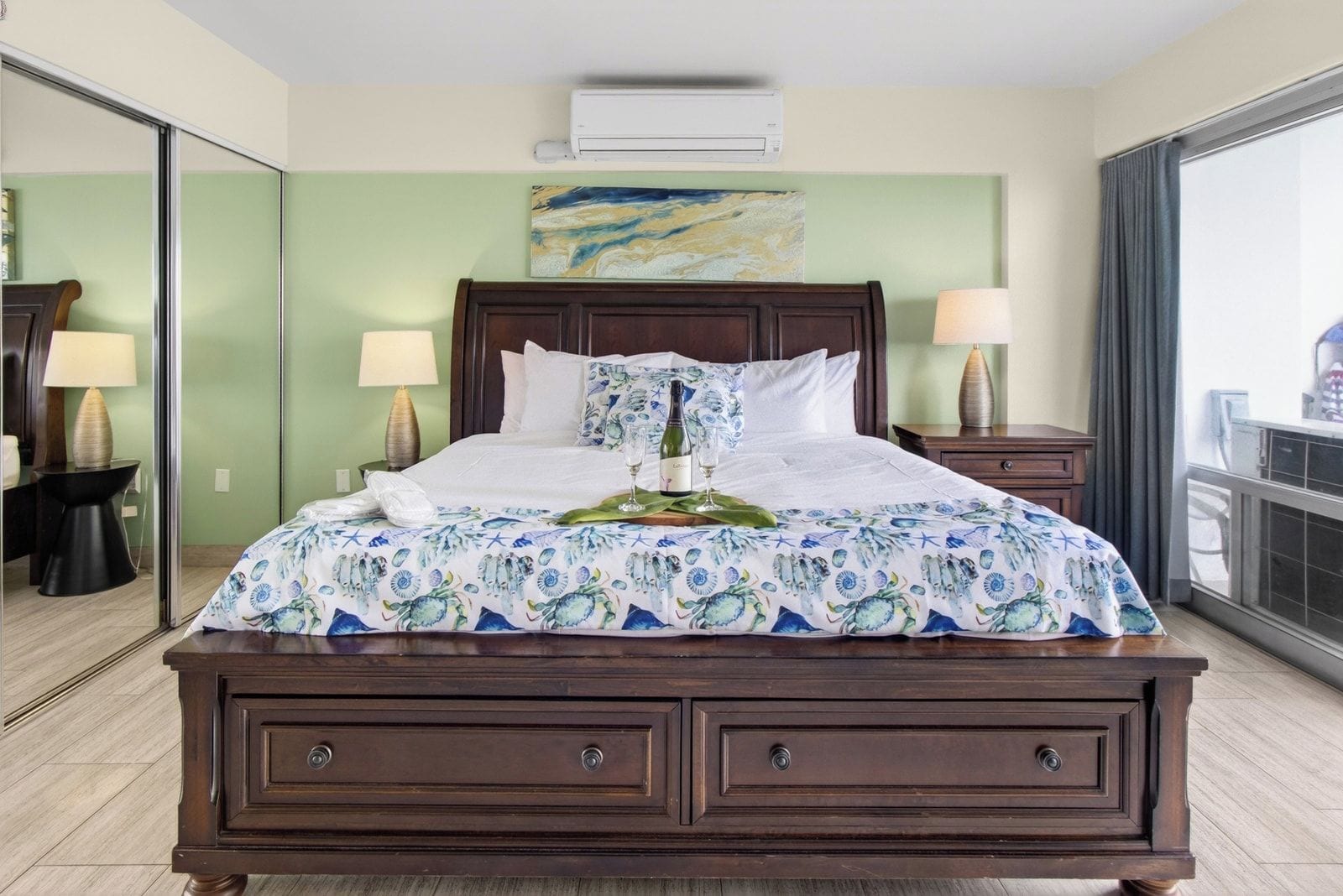 A hotel room with a large bed, a bedside table with a lamp, a mirror, and a window with curtains.