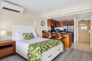 Ein Hotelzimmer mit Bett, Nachttisch, Lampe und einer Küchenzeile, inklusive Kühlschrank, Mikrowelle und Spüle.