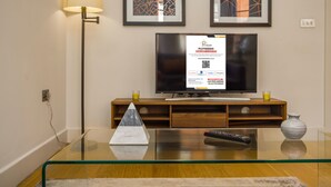 Una sala de estar con una mesa de centro de vidrio, un control remoto, un florero y un televisor sobre un mueble de madera.