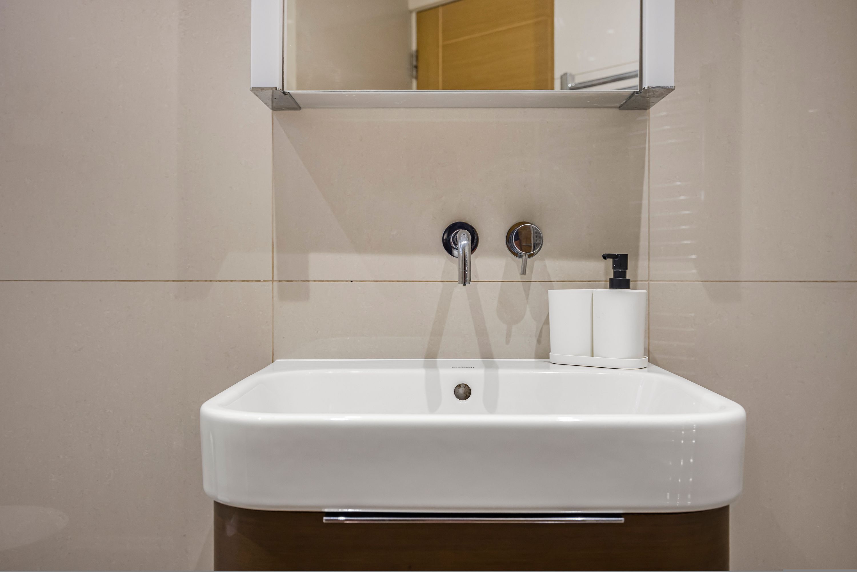 Een badkamer met een wit wastafel, twee kraan, een spiegel en een toiletrolhouder.