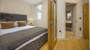 Un dormitorio con cama, ventana, puerta de madera y baño visible a través de una puerta abierta.