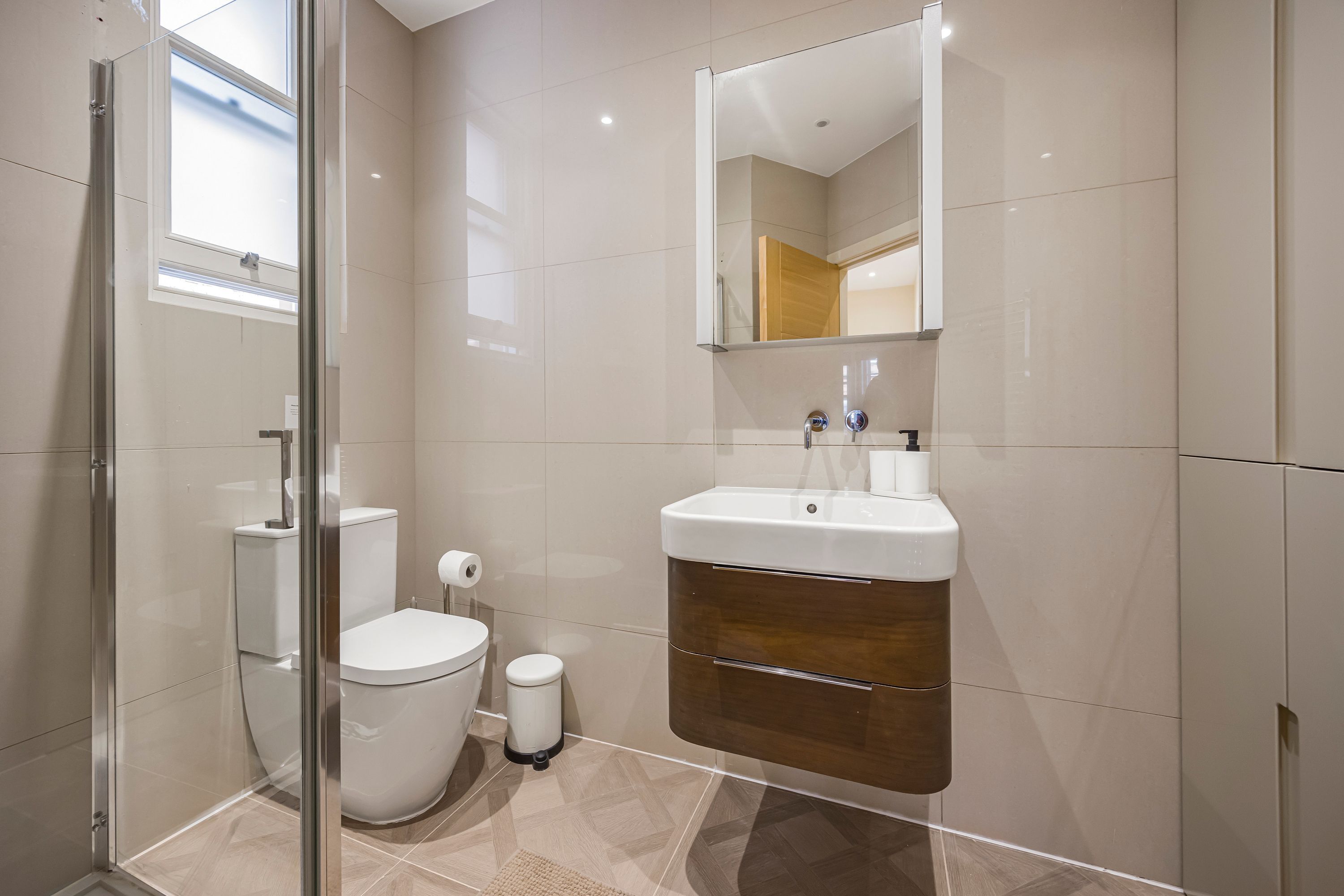 Un baño moderno con cabina de ducha de vidrio, inodoro, lavabo con espejo y dispensador de papel higiénico.