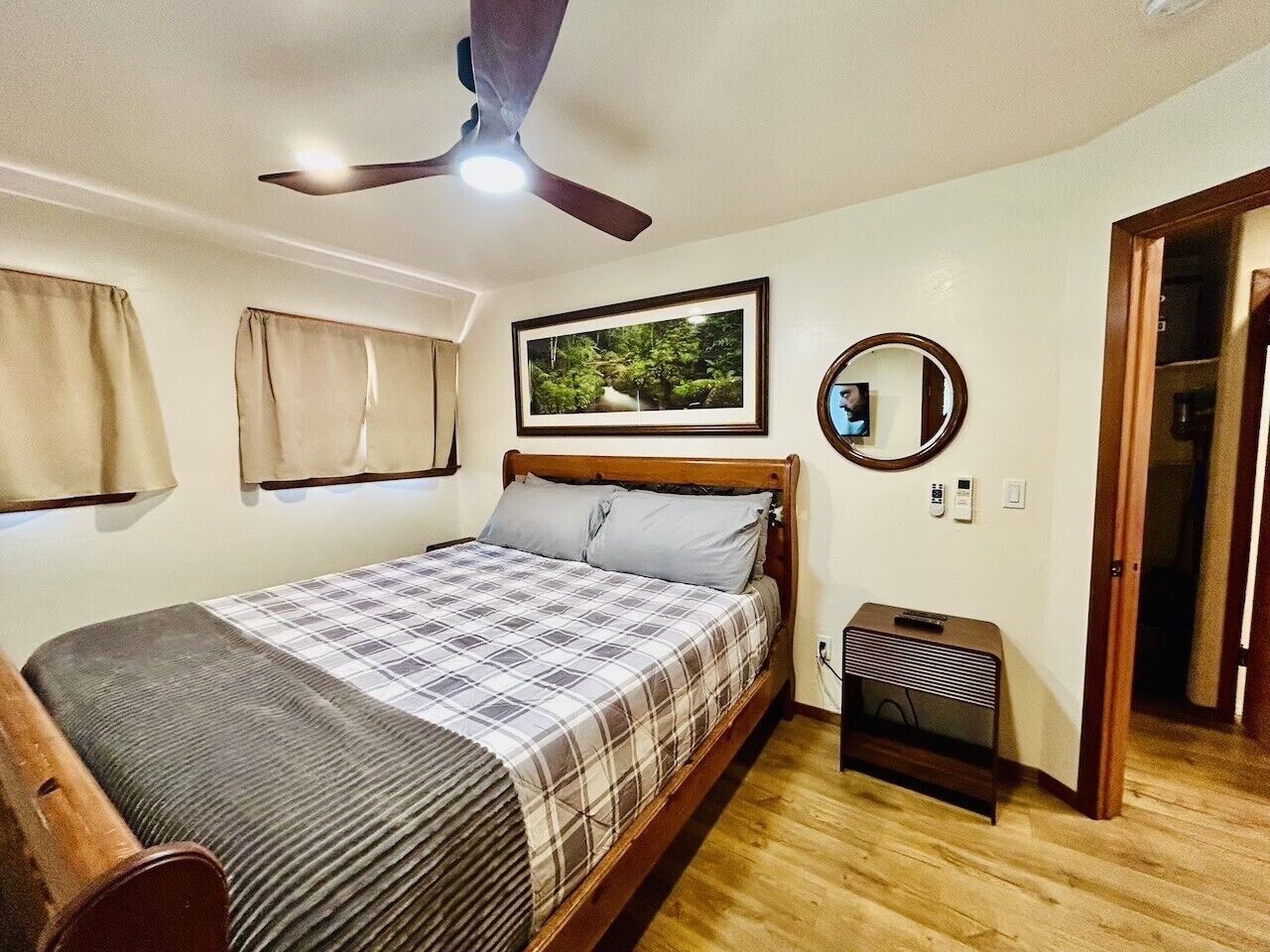 Une chambre à coucher avec un lit, un ventilateur de plafond, un tableau encadré, un miroir et une table de chevet.