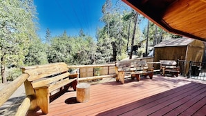 A wooden deck with benches and a covered area, surrounded by trees.