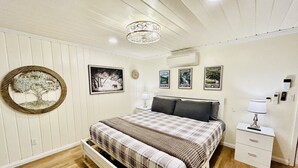 A bedroom with a bed, bedside tables, a wall clock, framed pictures, and a circular mirror.