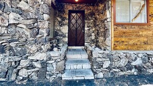 A stone-walled building with a wooden door and steps leading to a window with blinds.