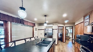 A kitchen with a large island, stainless steel appliances, wooden cabinets, and a hanging light fixture.