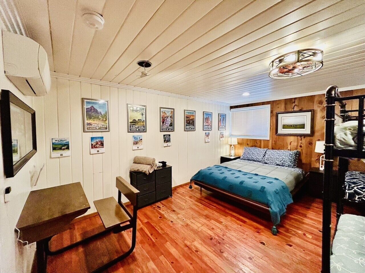 A room with a bed, a desk, a chair, a bunk bed, and wall-mounted pictures.