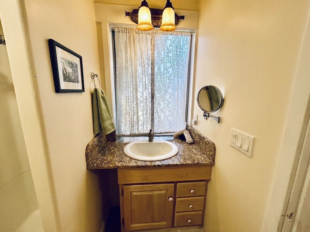 Un baño con lavamanos, tocador, espejo y ventana con cortinas.