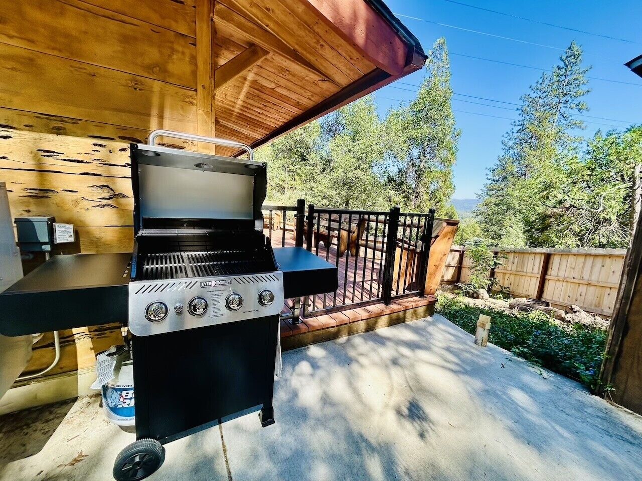 Una parrilla con tapa, una mesa y una terraza de madera con valla.