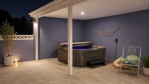 Ein überdachter Patio-Bereich mit Whirlpool, einem Sessel und einem Blumentopf.