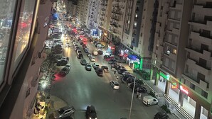 Nachts belebte Stadtstraße mit mehrstöckigen Gebäuden, geparkten Autos und beleuchteten Schaufenstern.