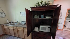 Una cocina con microondas, armarios, un lavabo y un reloj.