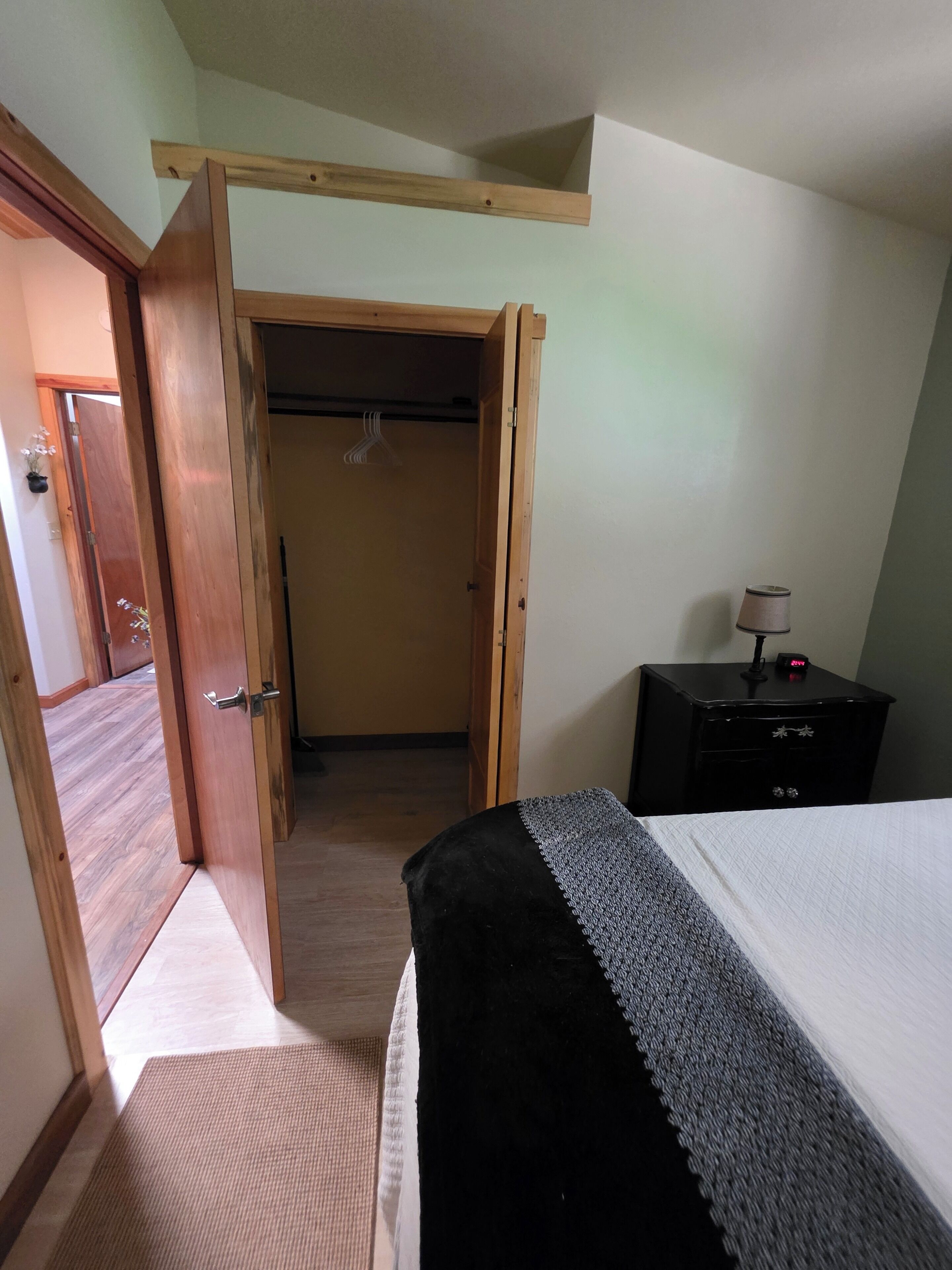 A bedroom with a bed, a nightstand, a wooden wardrobe, and a door leading to another room.