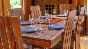 Una mesa de comedor de madera dispuesta con platos, cubiertos y copas de vino, rodeada de sillas de madera.