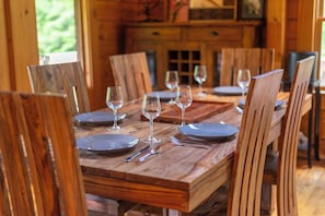 Ein Holztisch ist mit Tellern, Besteck und Weingläsern gedeckt und von Holzstühlen umgeben.