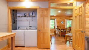 Interior de madera con zona de lavandería, puertas de madera y comedor con sillas.