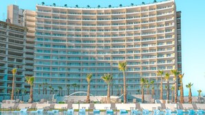 Un grand hôtel doté de nombreux balcons, d’une piscine et de palmiers.