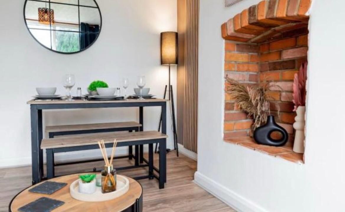 Un coin repas agrémenté d’une cheminée en briques, d’un miroir rond et d’une table dressée pour deux personnes.