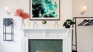 A room with a white fireplace, a clock, a framed abstract painting, and a wall-mounted light fixture. - NEW 3BR Stylish Home Near NEC | HS2 | JLR | Resorts World & B'ham Airport (Birmingham)