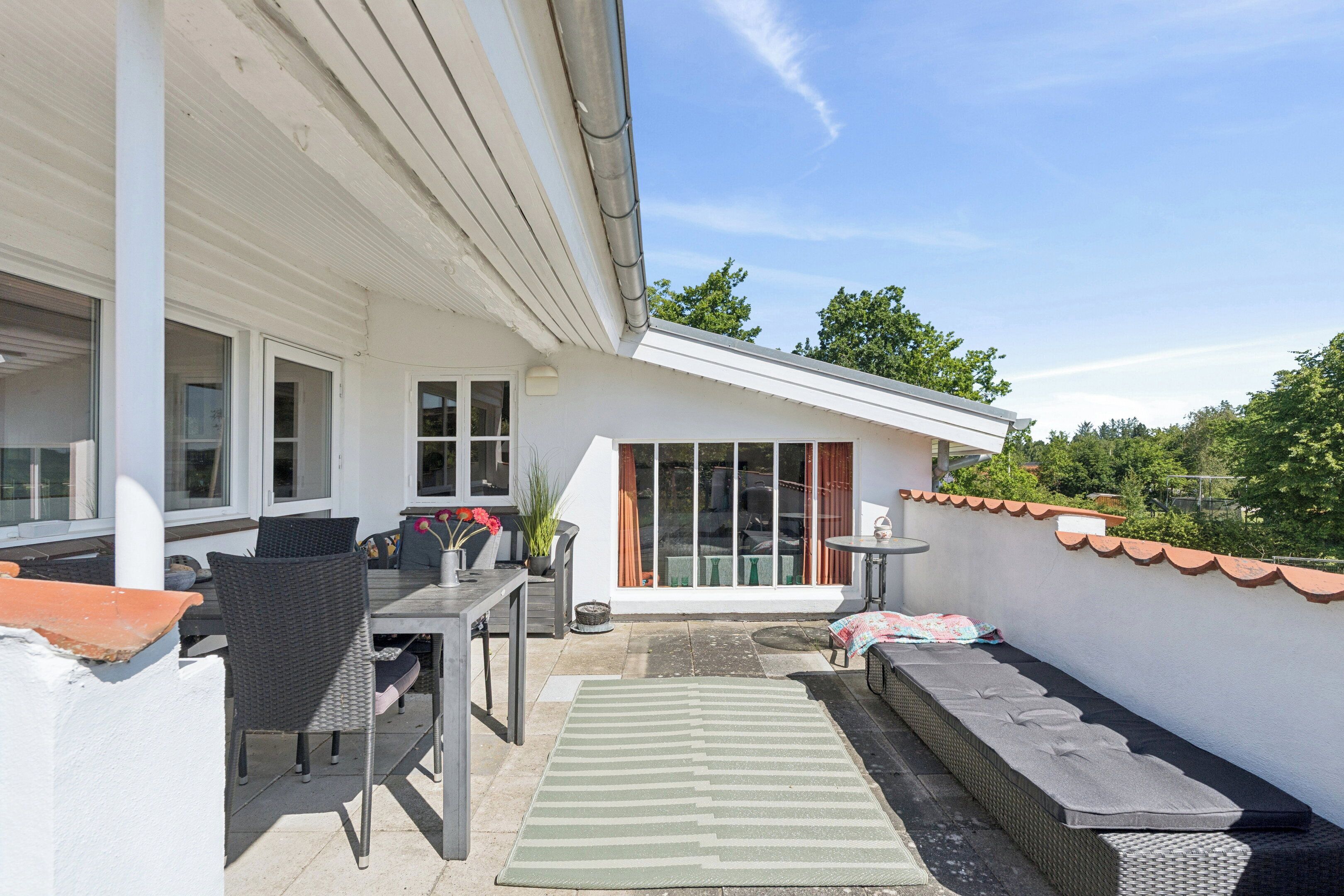 An outdoor patio with a dining table, chairs, a small rug, and a bench.