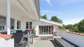 Eine Terrasse im Freien mit Esstisch, Stühlen, einer kleinen Matte und einer Bank.