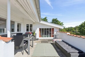 An outdoor patio with a dining table, chairs, a small rug, and a bench.