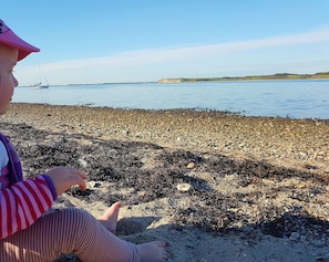 Ein Kind spielt an einem Kiesstrand mit ruhiger See und weit entfernten Hügeln.