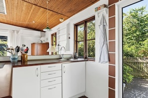 A kitchen with white cabinets, a wooden countertop, a window with a view of greenery, and a hanging towel.
