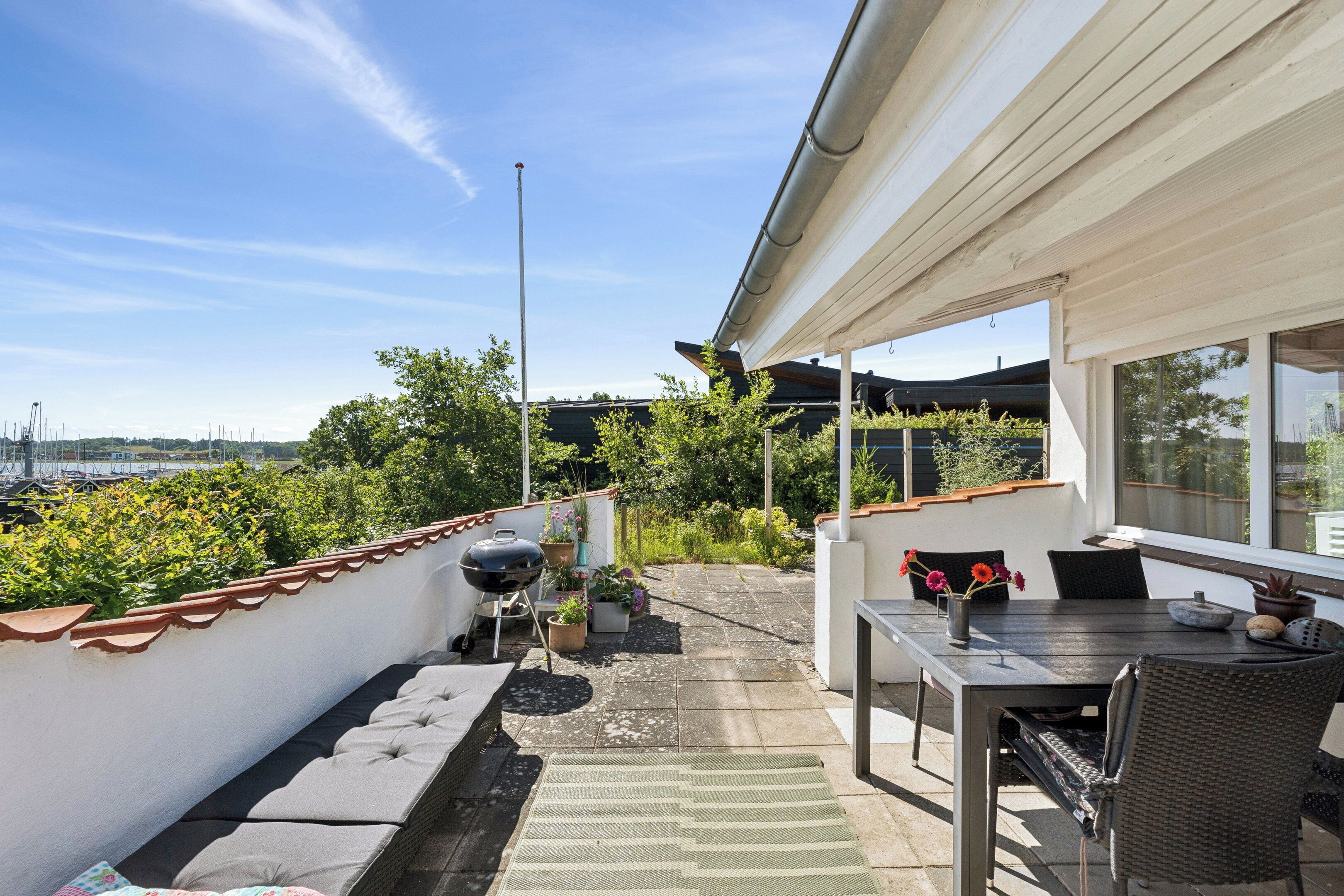Een terras op het dak met een eettafel, stoelen, een barbecue en een bank.