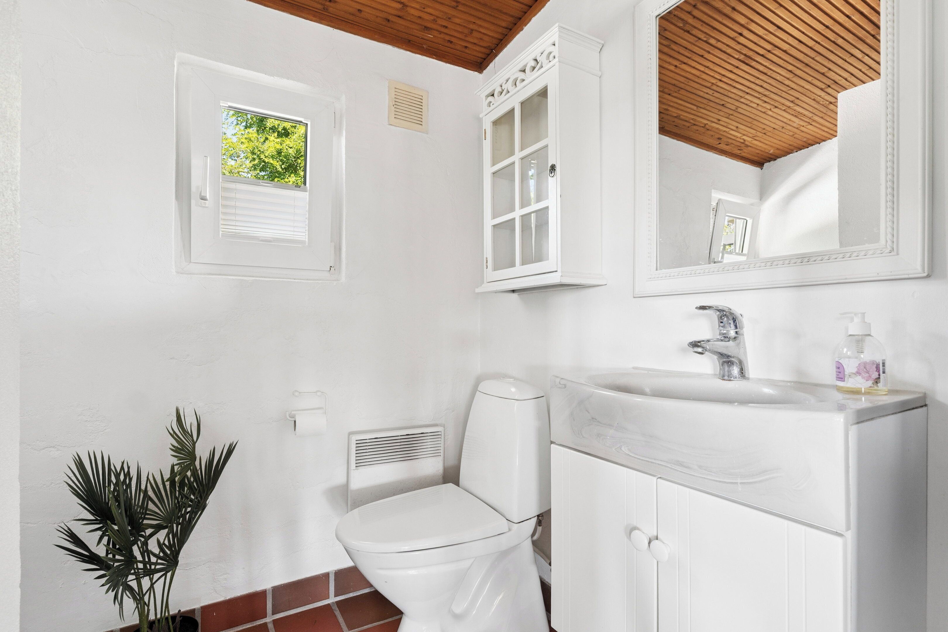 Et badeværelse med toilet, vask, spejl, vindue og en plante.