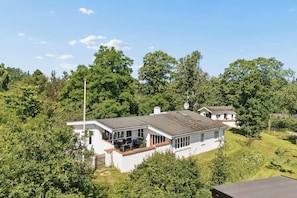 Ein weißes Haus mit grauem Dach, umgeben von üppiger Vegetation und Bäumen.