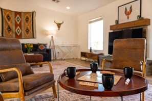 A cozy living room with two leather armchairs, a round coffee table with a Scrabble game, and a fireplace. - Sun & Rally Retreat | Dual Swim Spa | Pickleball (Yucca Valley)