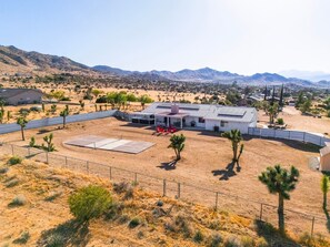Una casa con patio cercado, terraza techada y paisaje desértico con montañas al fondo.