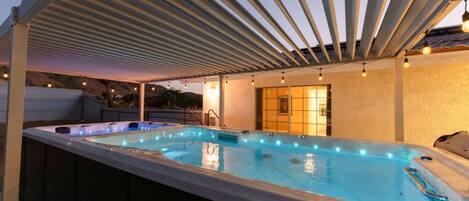 Un espace extérieur avec un jacuzzi, agrémenté d’une pergola couverte, d’un coin salon et offrant une vue sur le paysage.