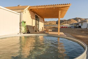 Una piscina con una pérgola de madera, sillas de descanso y vistas a un paisaje montañoso.