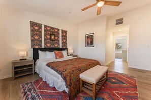Une chambre à coucher comprenant un lit, des tables de chevet, un banc, un ventilateur de plafond et des décorations murales à motifs.