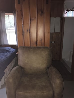 A room with a bed, a wooden wardrobe, a chair, and a bathtub.