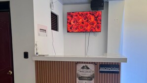 En receptionsdisk med en väggmonterad tv, en skylt med texten ”RECEPTION” och ett mönstrat golv.