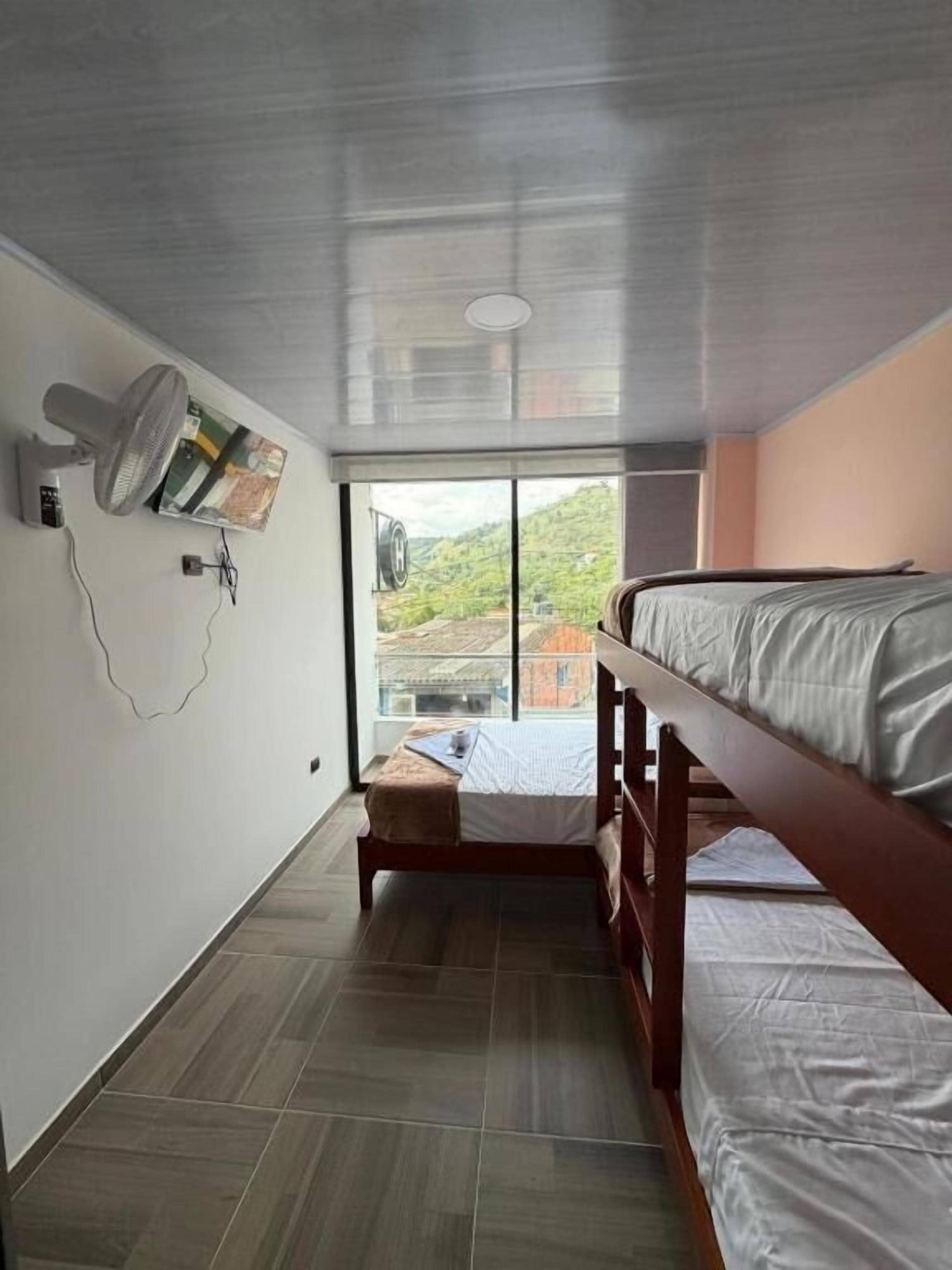 A room with a bunk bed, a fan, a window, and a view of the outdoors.
