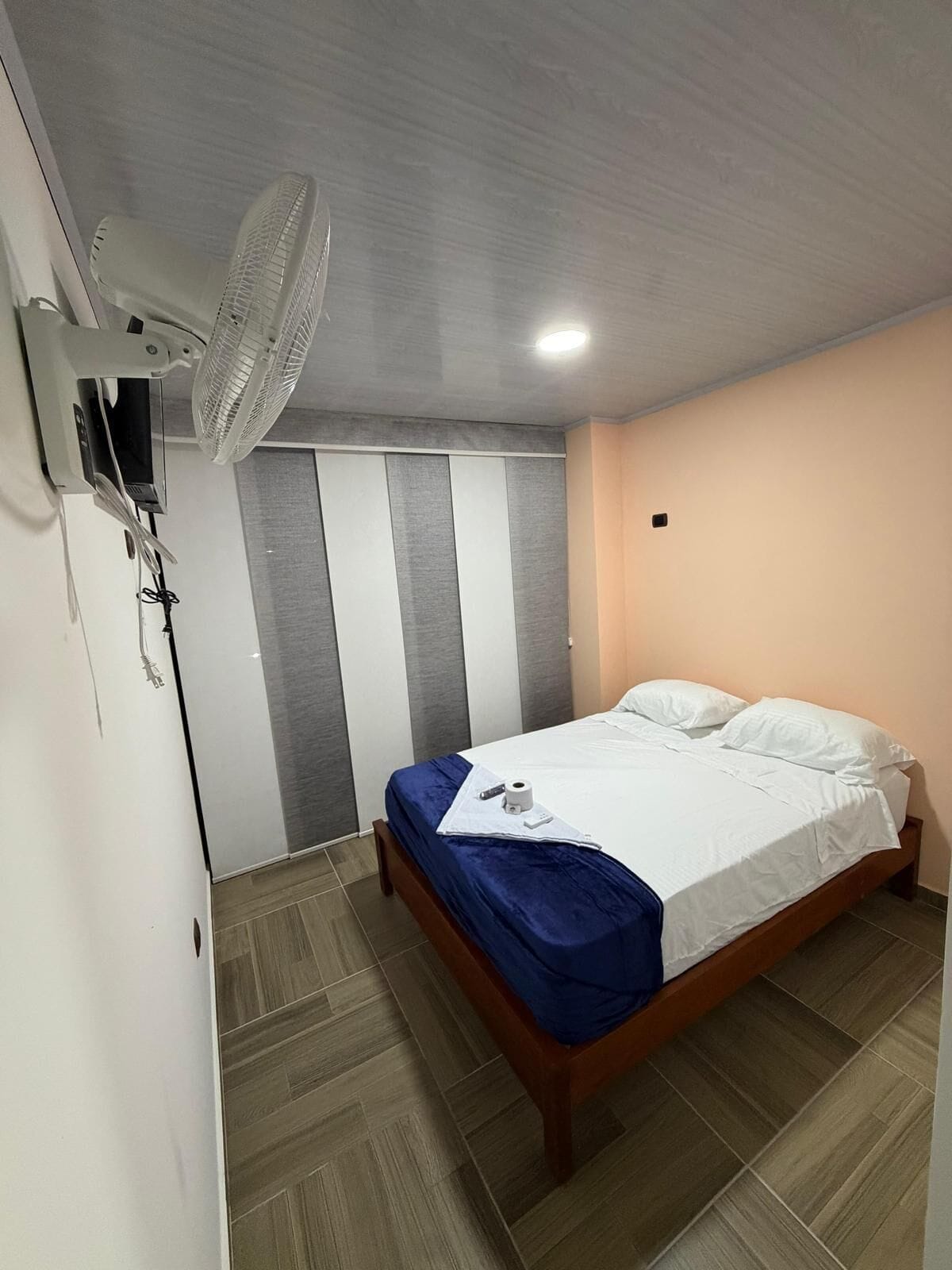 A bedroom with a bed, a ceiling fan, a TV, and a wardrobe.