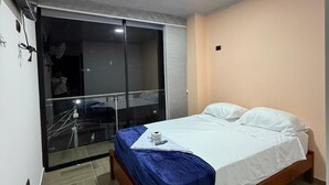 Ett hotellrum med en säng, en fläkt, en balkong med en glasdörr och en taklampa.